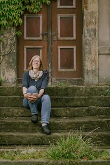 Sabine Adam sitzt auf einer Treppe vor einer alten Holztür